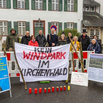 Eine Gruppe steht hinter einem Transparent, auf dem steht: „Kein Windpark im Kirchenwald“.