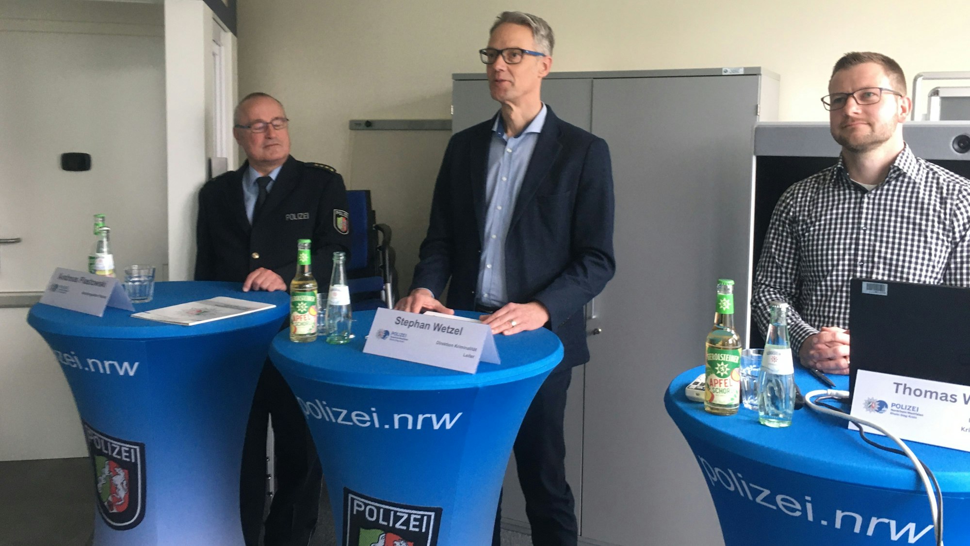 Drei Männer stehen an Stehtischen und präsentieren polizeiliche Ergebnisse.