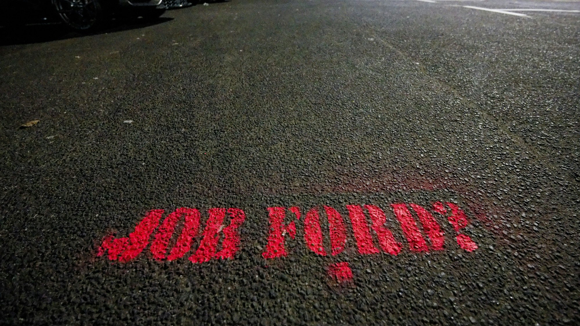Auf dem Asphalt eines Parkplatzes vor den Fordwerken steht "Job Ford?".