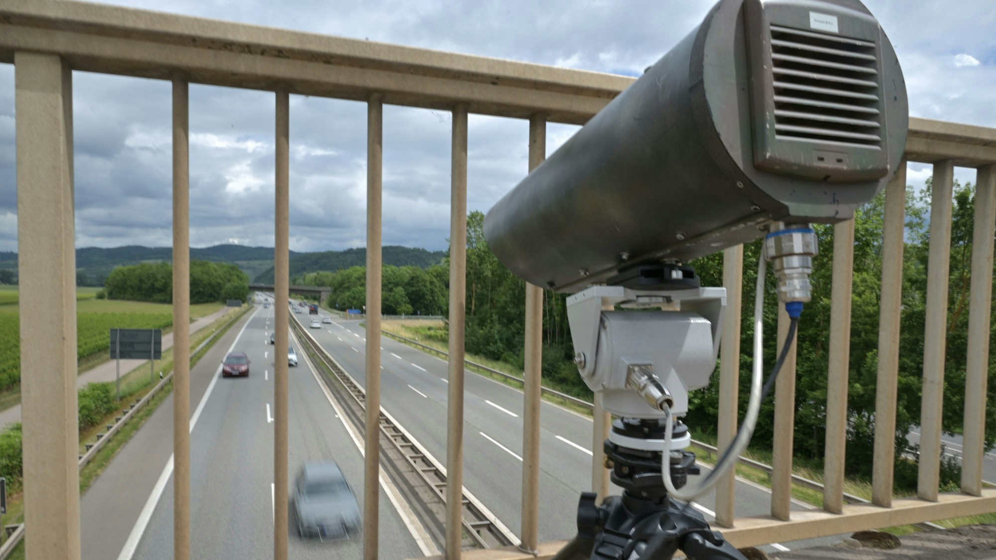 Eine Monocam steht auf einer Brücke, die über eine Autobahn führt.