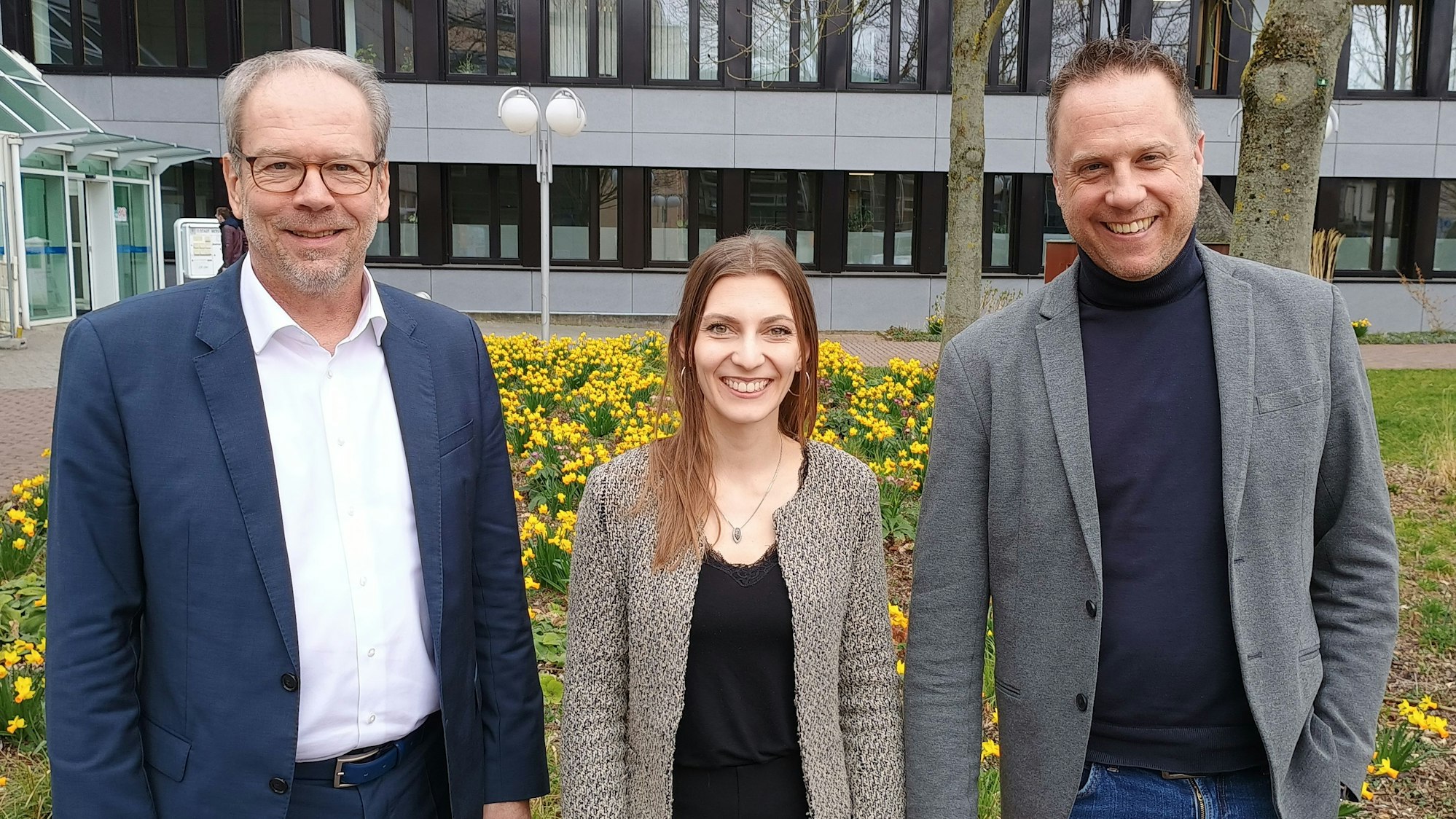 Die drei stehen vor dem Bergheimer Rathaus und lächeln in die Kamera.