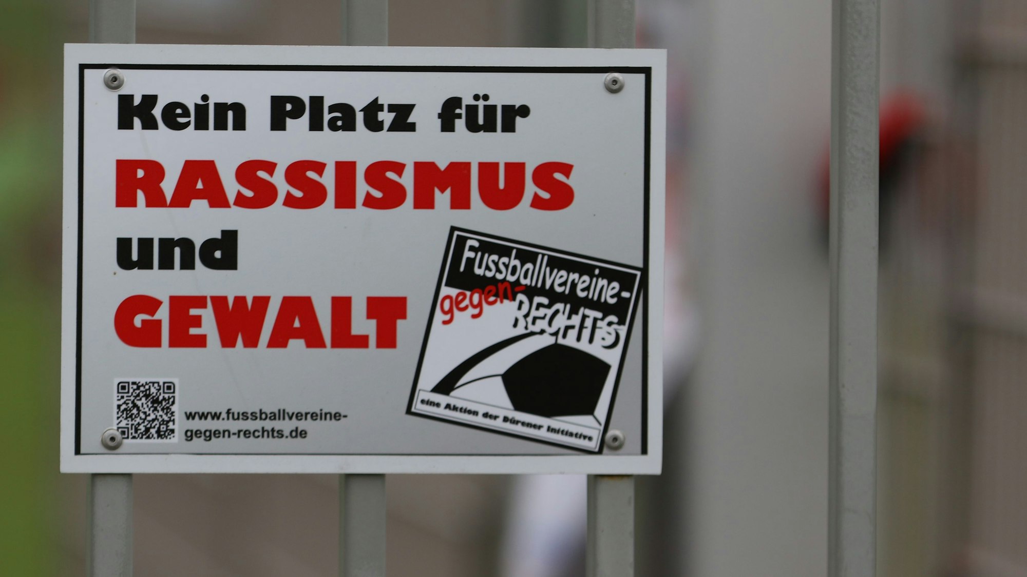 Auf einem Schild an einem Sportplatzzaun steht „Kein Platz für Rassismus und Gewalt“.