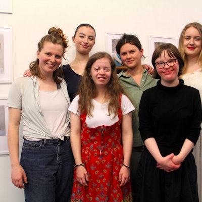 Sechs junge Frauen stehen vor einer Wand mit Bildern