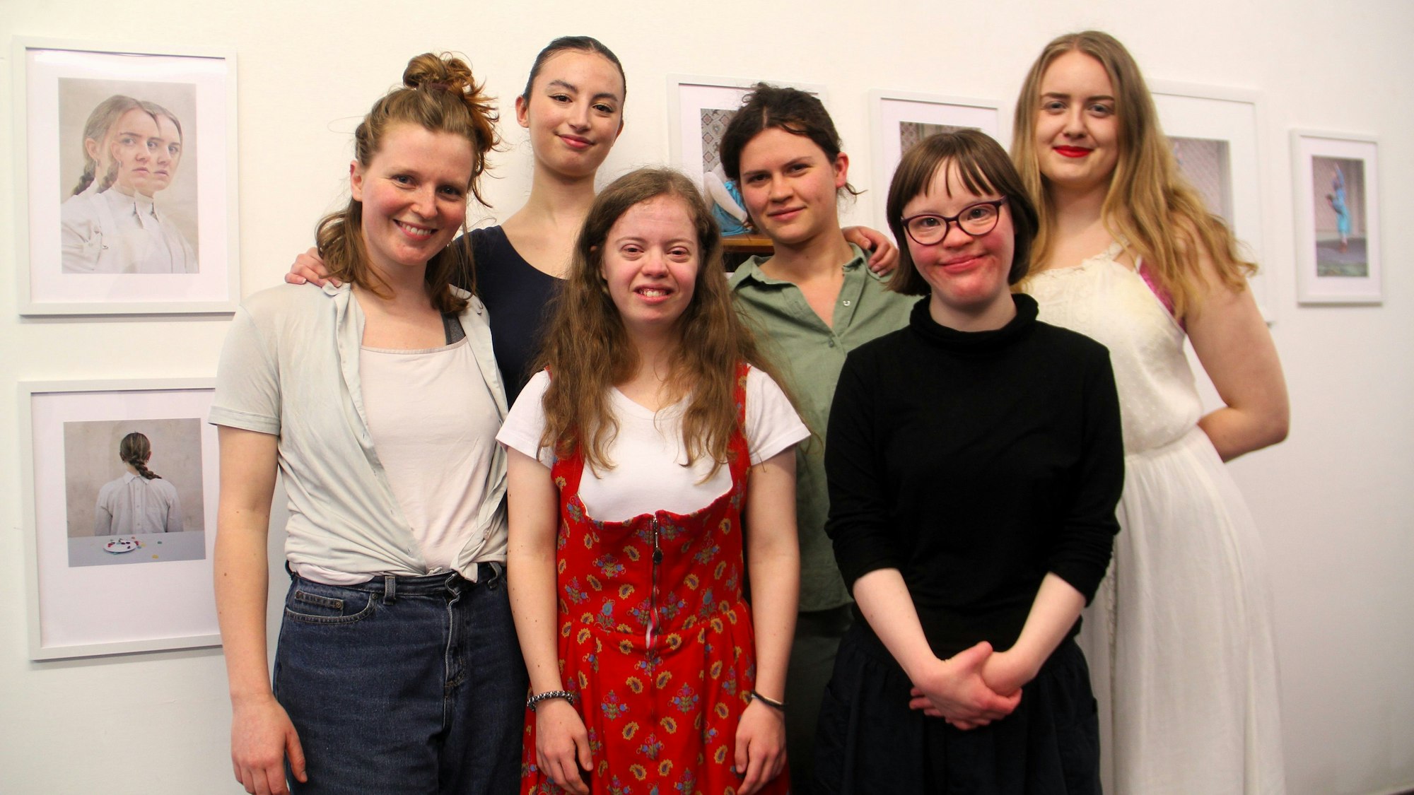 Sechs junge Frauen stehen vor einer Wand mit Bildern