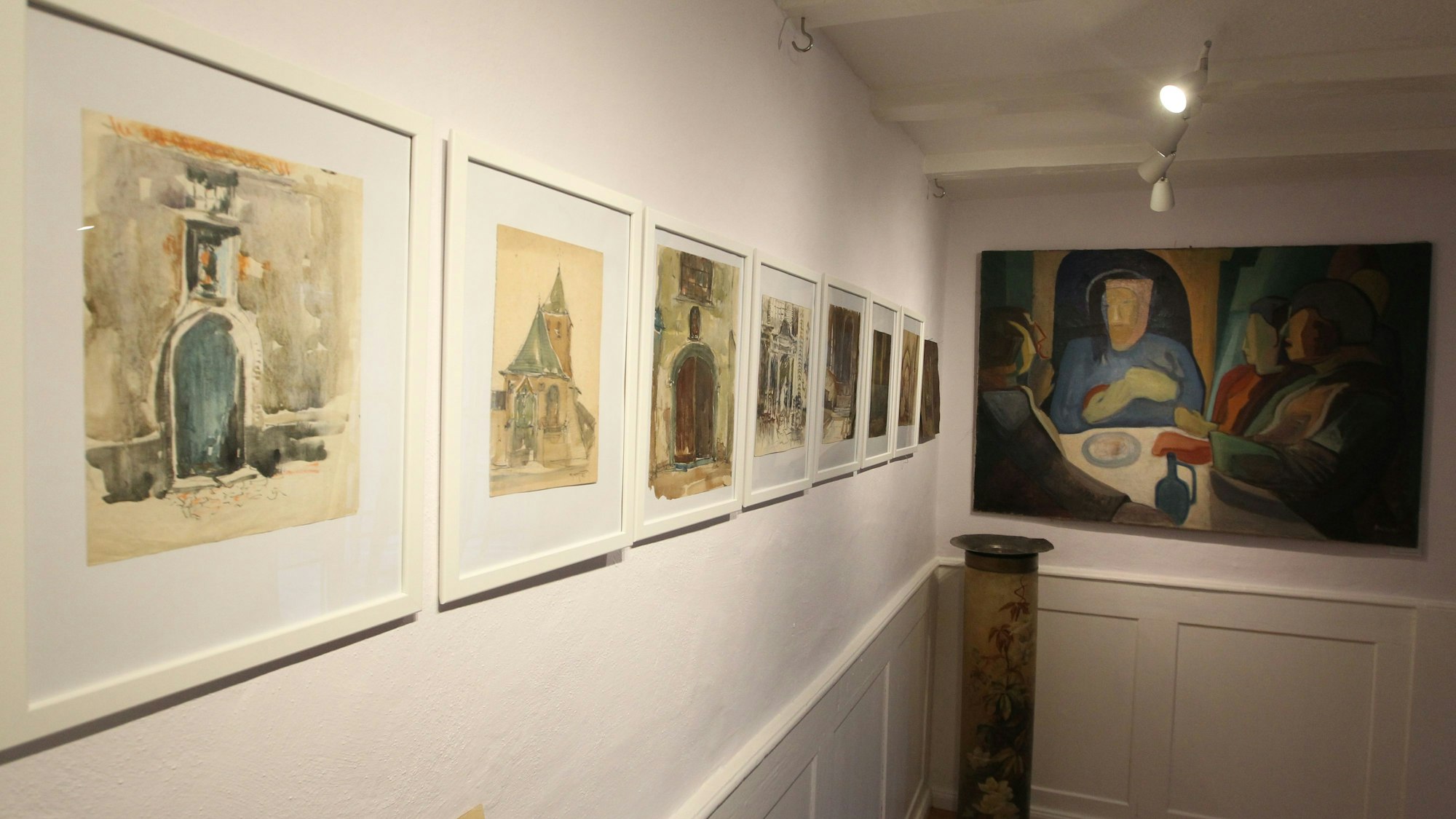 Der Blick in einen Ausstellungsraum mit Aquarellen und Gemälden an der Wand.