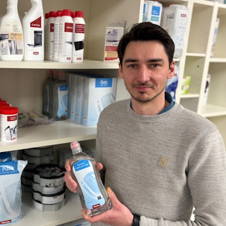 Auf dem Bild ist ein Mann zu sehen, der ein Pflegeprodukt für Spülmaschinen hält.