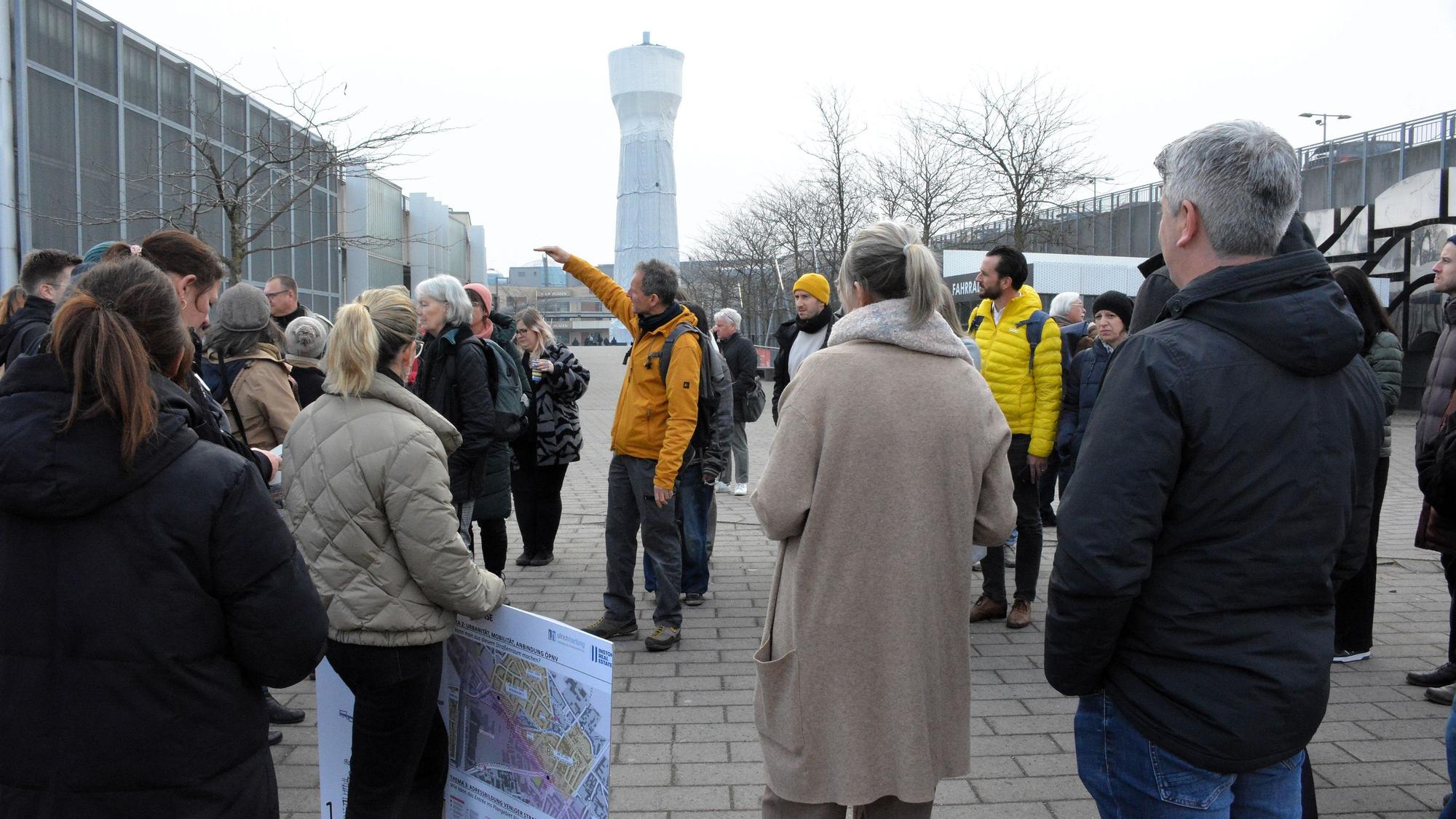 Eine Gruppe von Menschen diskutiert vor einem Wasserturm.