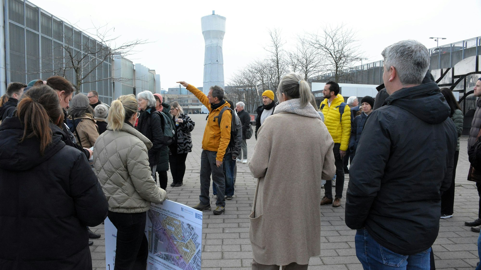 Eine Gruppe von Menschen diskutiert vor einem Wasserturm.