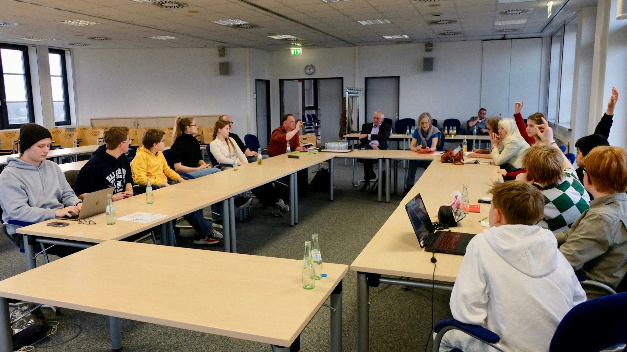 Jugendliche und Erwachsene sitzen in einem Sitzungssaal an Tischen zusammen.