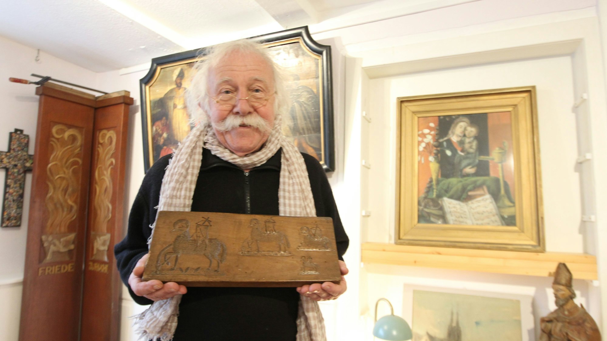 Ein Mann mit weißen Haaren hat eine hölzerne Backform in der Hand.