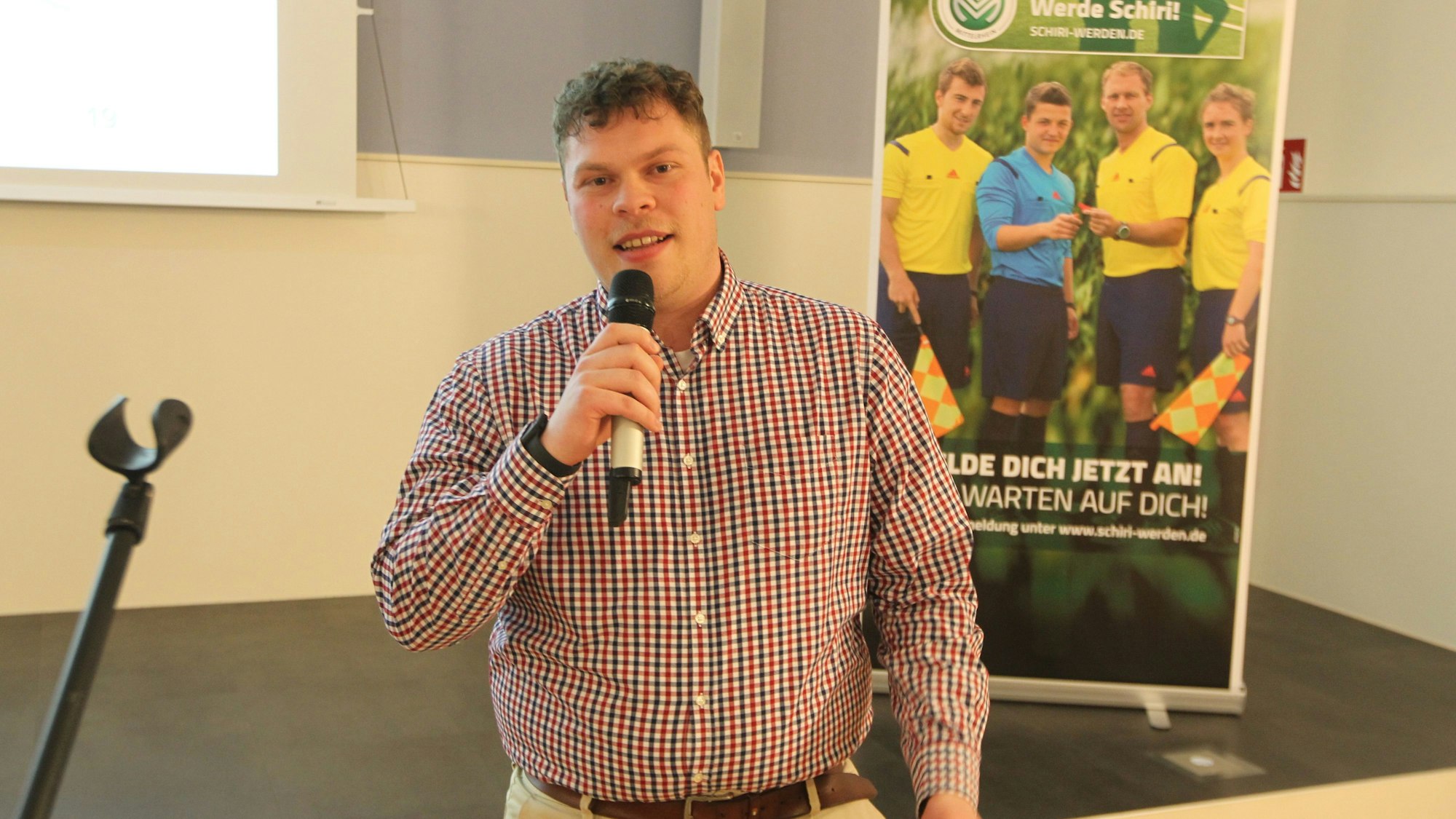 Ein junger Mann im karierten Hemd spricht in ein Mikrofon.