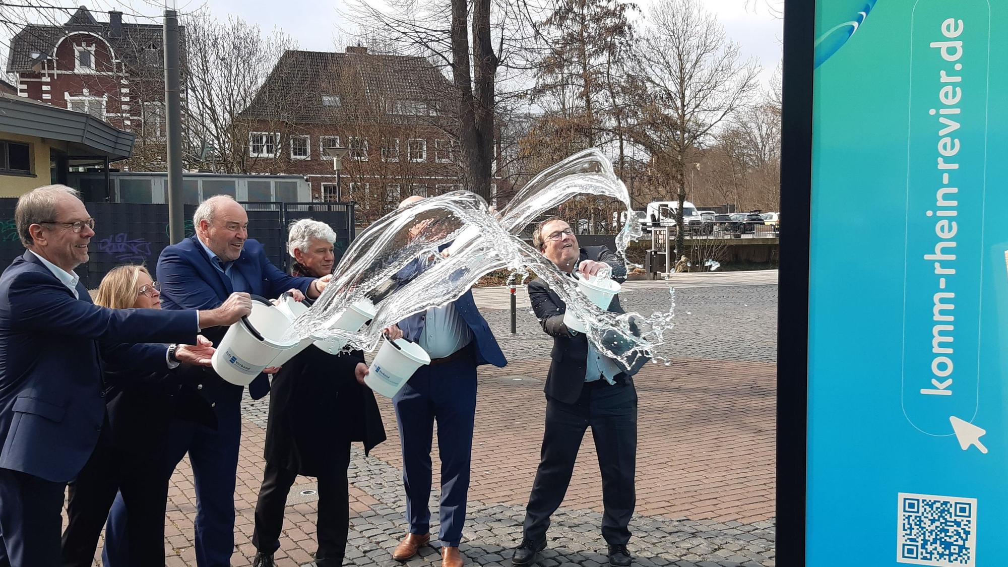 Zu sehen sind NRW-Umweltminister Oliver Krischer, Landrat Frank Rock, Bergheims Bürgermeister Volker Mießeler und Vertreter des Erftverbandes, die Eimer Wasser ausschütten.