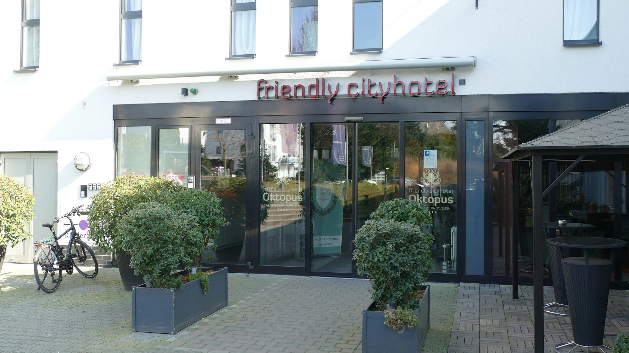 Vorplatz und Eingang eines Hotels. Über der Tür hängt der Schriftzug "Friendly Cityhotel"