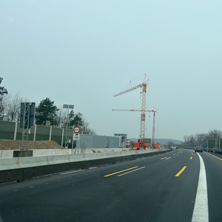 Auf dem Mittelstreifen einer Autobahn stehen zwei Kräne.