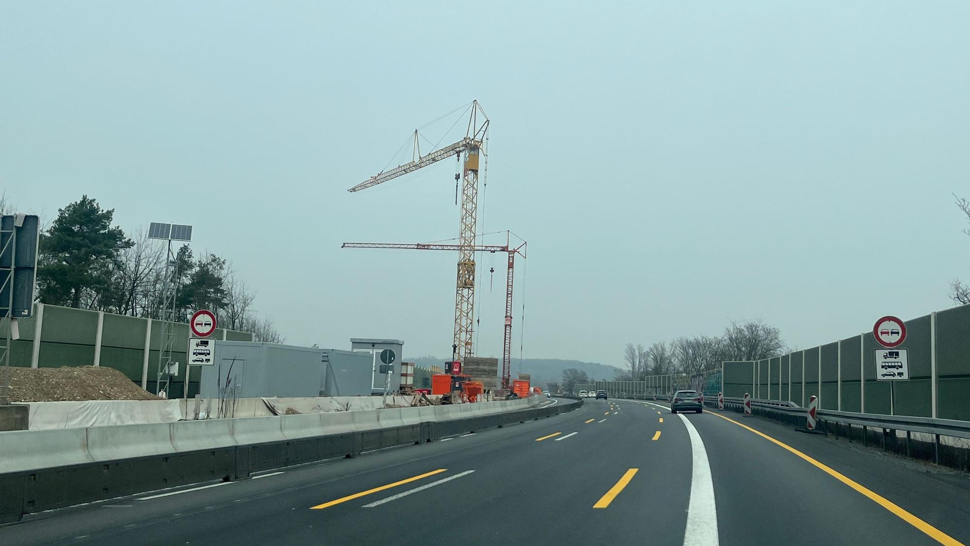 Auf dem Mittelstreifen einer Autobahn stehen zwei Kräne.