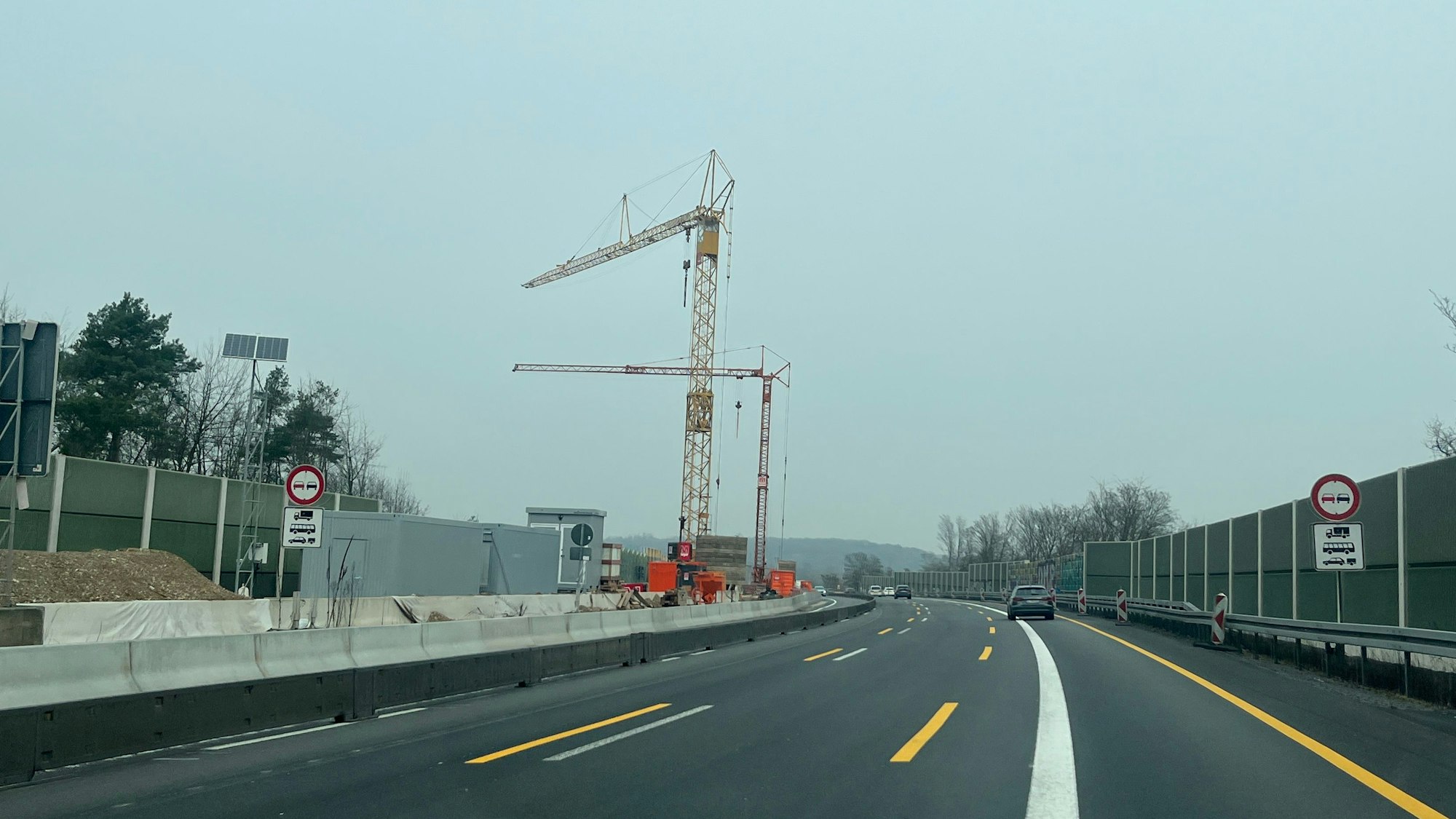 Auf dem Mittelstreifen einer Autobahn stehen zwei Kräne.
