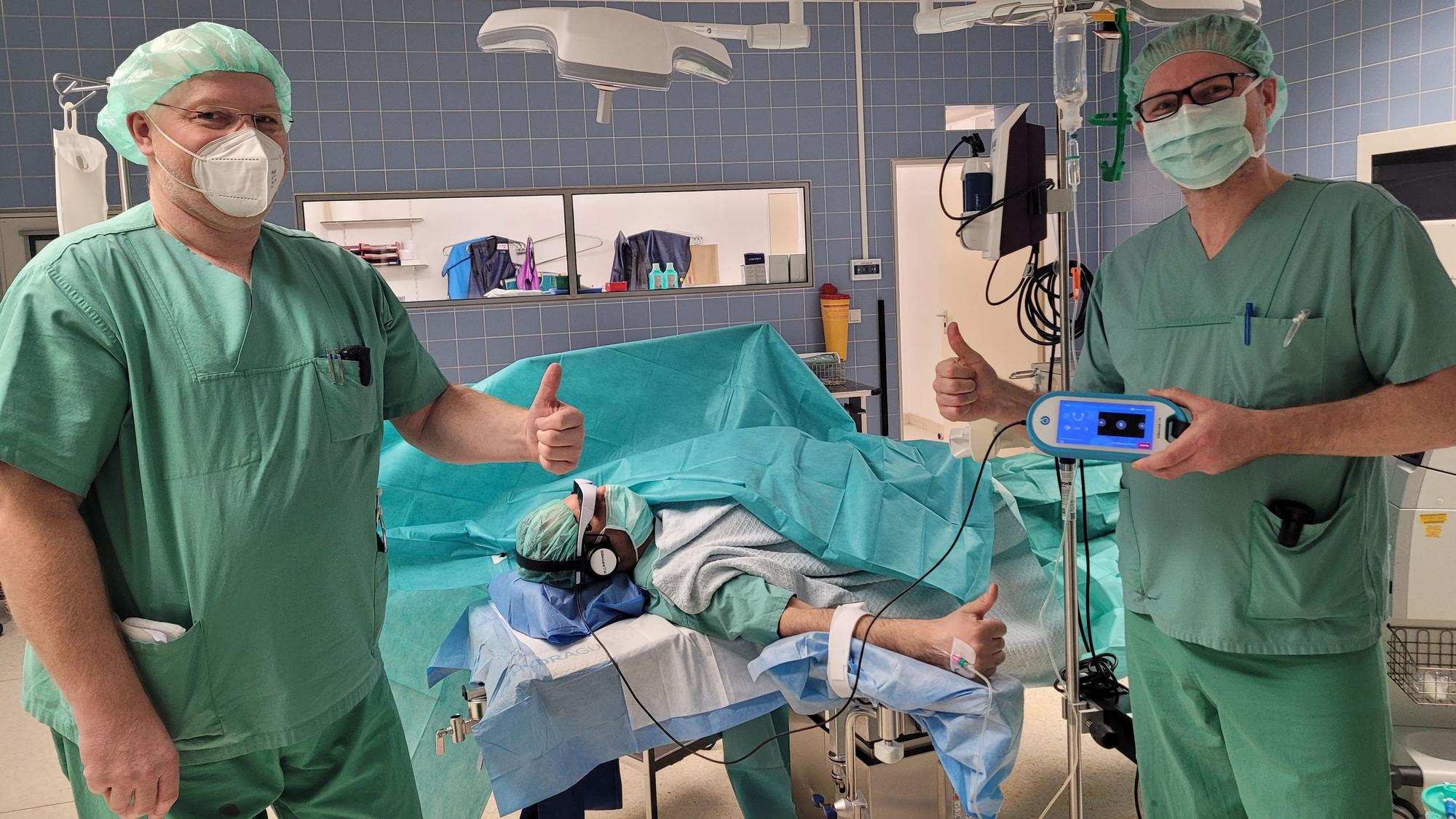Zwei Ärzte stellen eine VR-Brille für Patienten in einem OP-Saal vor.