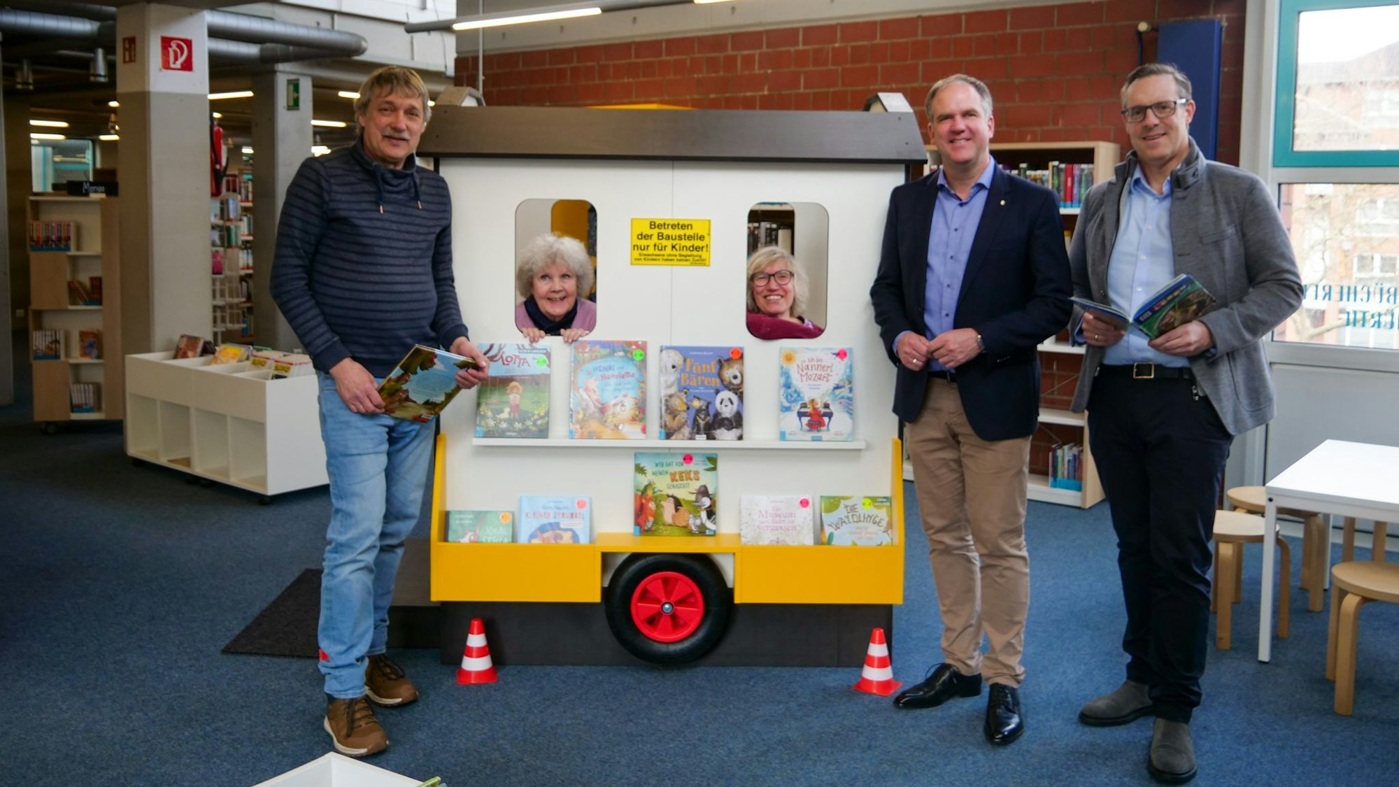 Zu sehen sind zwei Frauen und drei Männer in einer Bücherei.