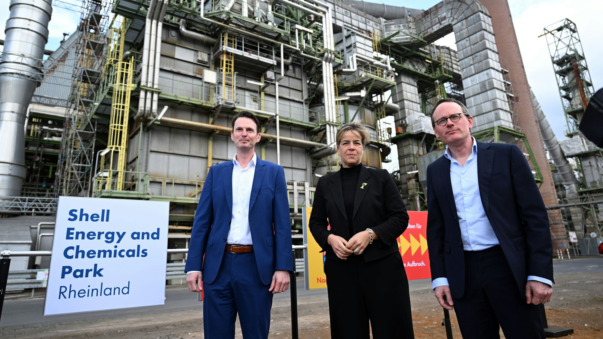 Mona Neubaur (Bündnis 90/Die Grünen, M), Ministerin für Wirtschaft, Industrie, Klimaschutz und Energie des Landes Nordrhein-Westfalen, Marco Richrath, Senior Vice President Chemical & Products Northwest EU (l), und Jan-Peter Root Wassink, General Manager Energy an Chemicals Park Rheinland (r), stehen vor einer Shell Destillationsanlage, die abgeschaltet wird.