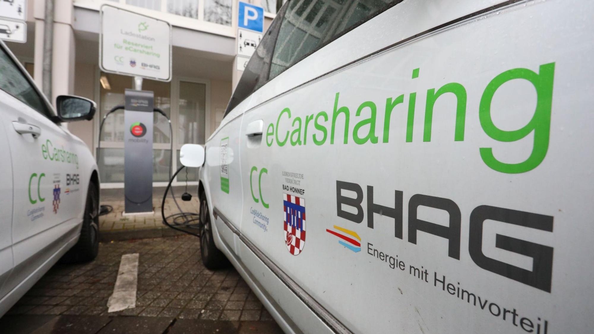 Zwei weiße Pkw mit der Aufschrift E-Carsharing vor einer Ladestation.