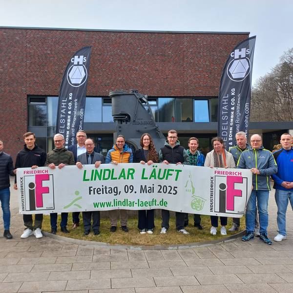 Vor dem historischen Schmiedehammer der Firma Höver präsentieren Organisatoren und Sponsoren von „Lindlar läuft“ das aktuelle Banner.