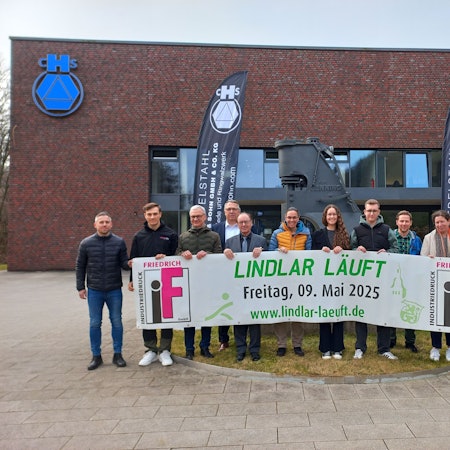 Vor dem historischen Schmiedehammer der Firma Höver präsentieren Organisatoren und Sponsoren von „Lindlar läuft“ das aktuelle Banner.