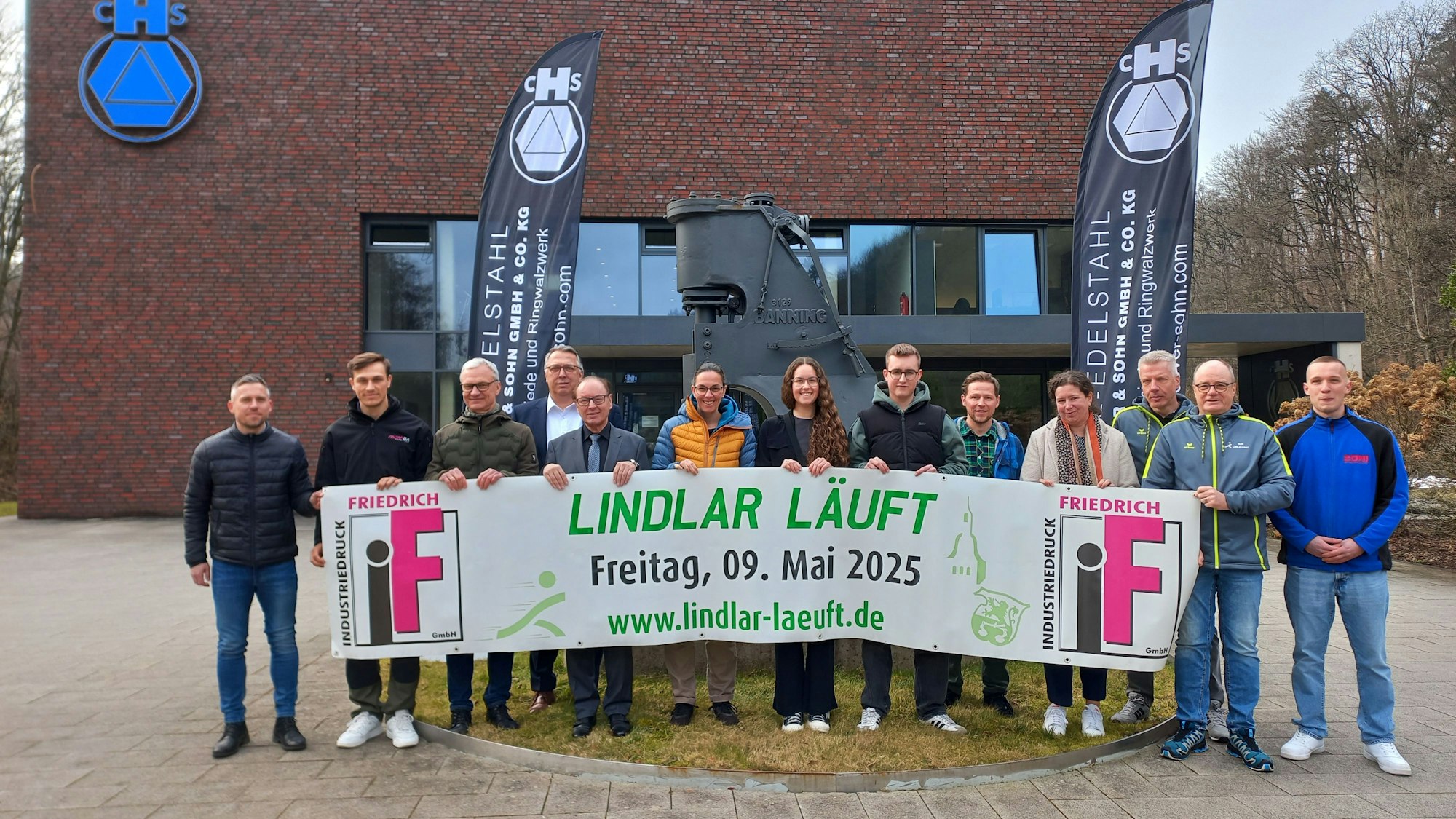 Vor dem historischen Schmiedehammer der Firma Höver präsentieren Organisatoren und Sponsoren von „Lindlar läuft“ das aktuelle Banner.