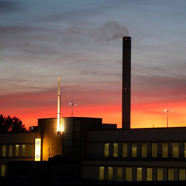 Der Schornstein des Isover-Werks in Bergisch Gladbach raucht vor dem Sonnenuntergangshimmel vor sich hin.