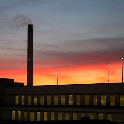 Der Schornstein des Isover-Werks in Bergisch Gladbach raucht vor dem Sonnenuntergangshimmel vor sich hin.