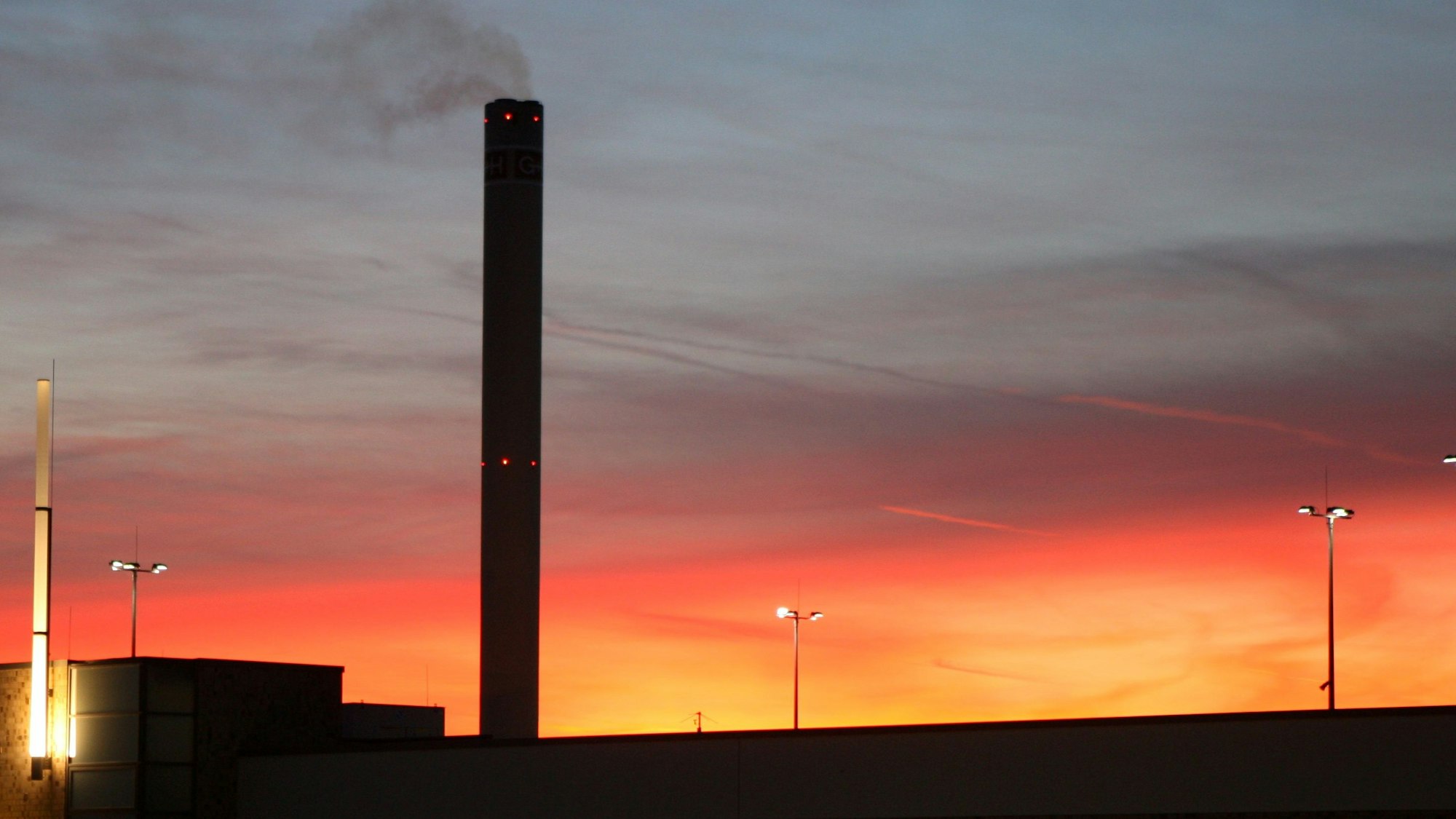 Der Schornstein des Isover-Werks in Bergisch Gladbach raucht vor dem Sonnenuntergangshimmel vor sich hin.