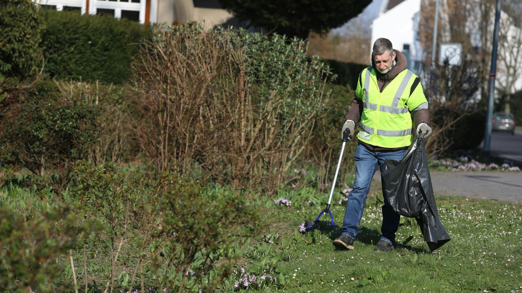 Ein Mann mit Warnweste, Müllsack und Zange sammelt Müll auf einer Wiese.