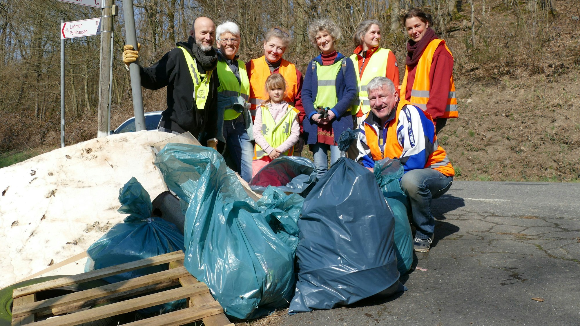 Menschen in Warnwesten stehen hinter einem großen Haufen Müll.