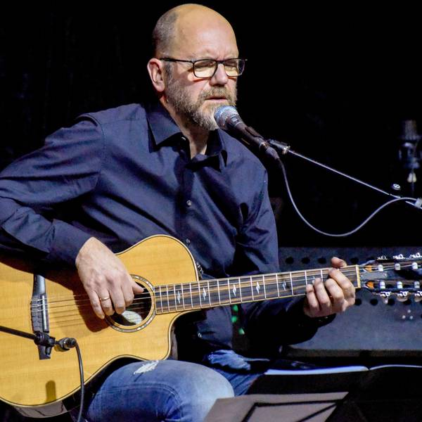 Ein Mann sitzt mit einer Gitarre auf einer Bühne.