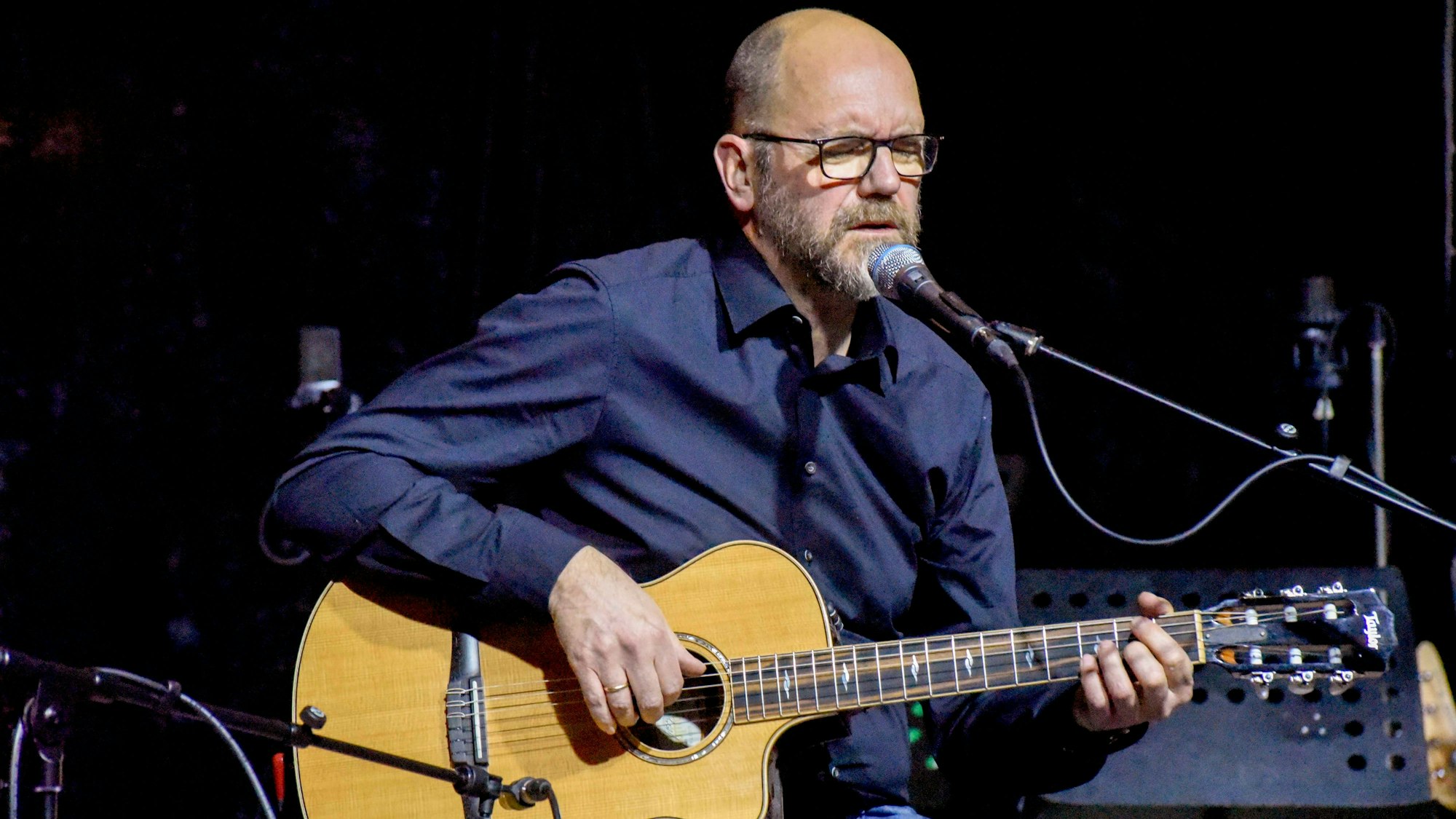 Ein Mann sitzt mit einer Gitarre auf einer Bühne.