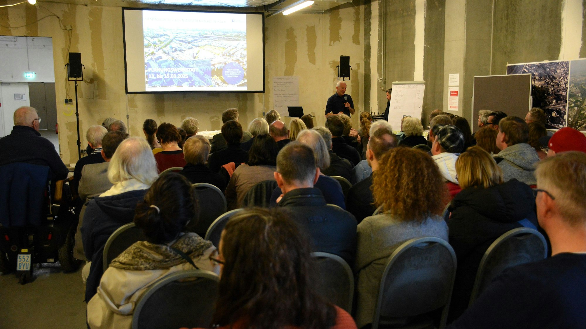 Menschen sitzen auf Stühlen vor einer Leinwand.