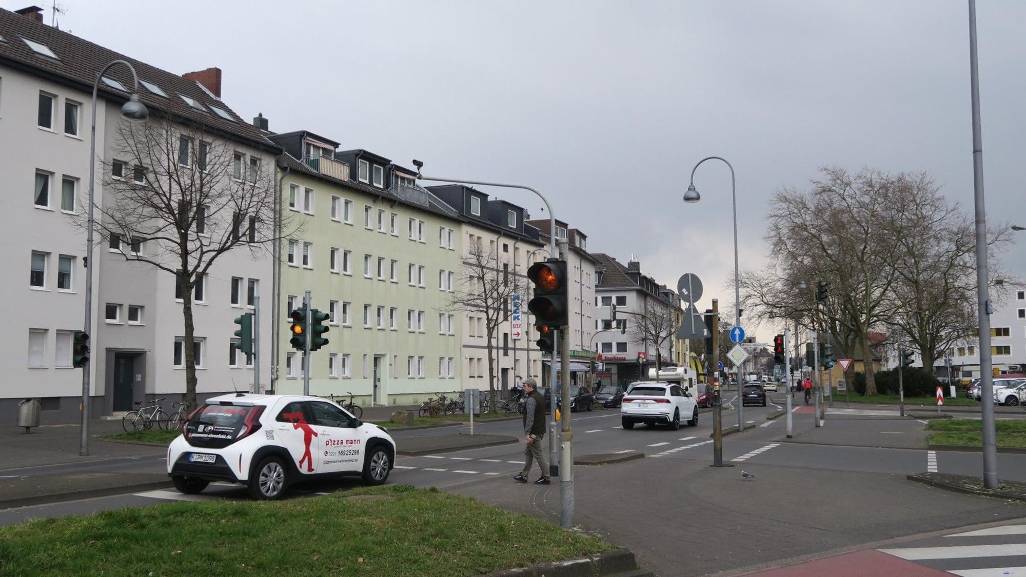 Autos fahren über eine Straße, ein Fußgänger will an einer Ampel die Straße überqueren.