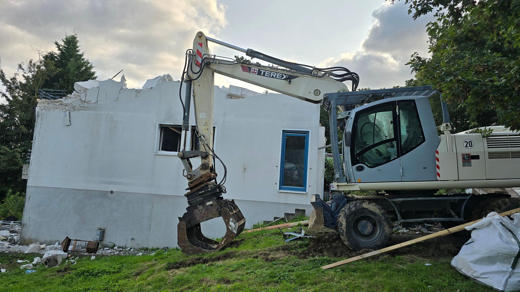 Das Foto zeigt einen Bagger bei den Abrissarbeiten, der Dachstuhl des Hauses fehlt.