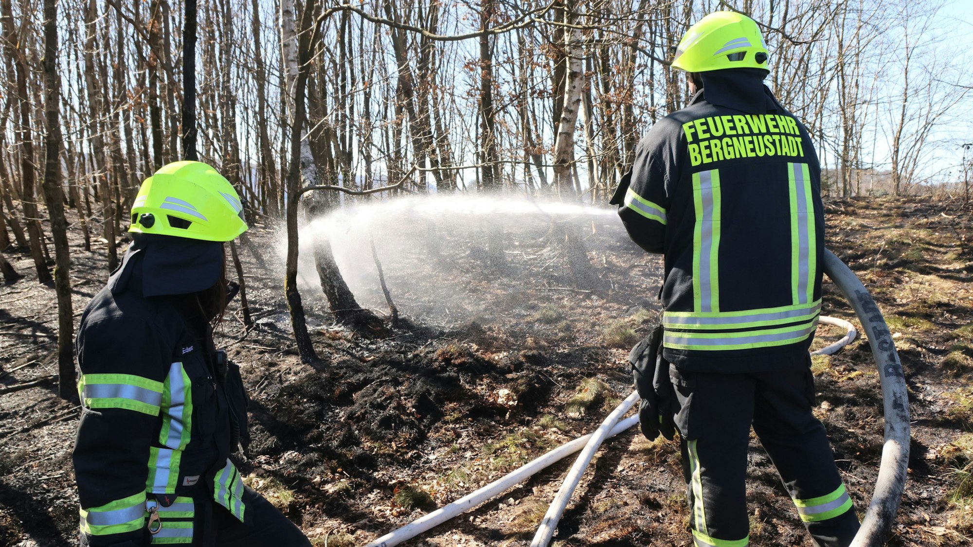 Zwei Feuerwehrleute löschen im Wald einen Brand.