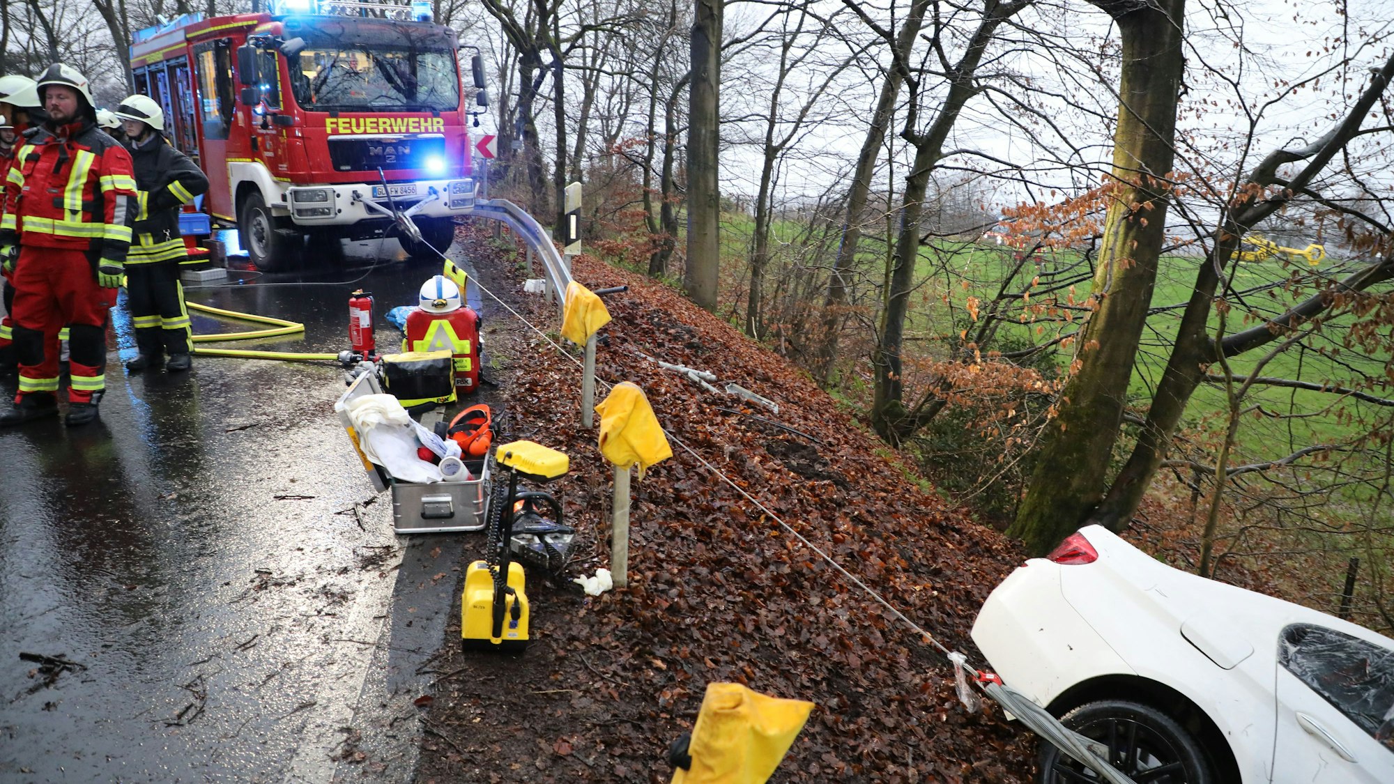 Ein von der Straße abgekommenes Auto wird von einem Feuerwehrfahrzeug mithilfe eines Seils gesichert.
