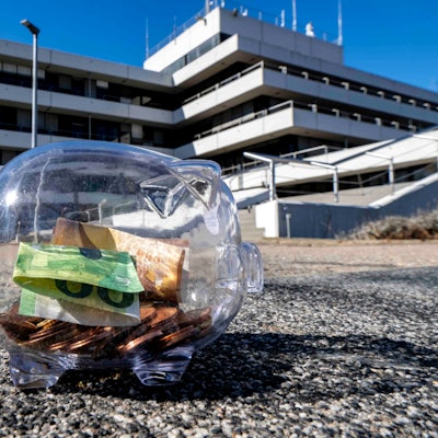 Das Bild zeigt ein Sparschwein auf der Treppe vor dem Kreishaus. Es ist mit Münzen und Scheinen gefüllt.