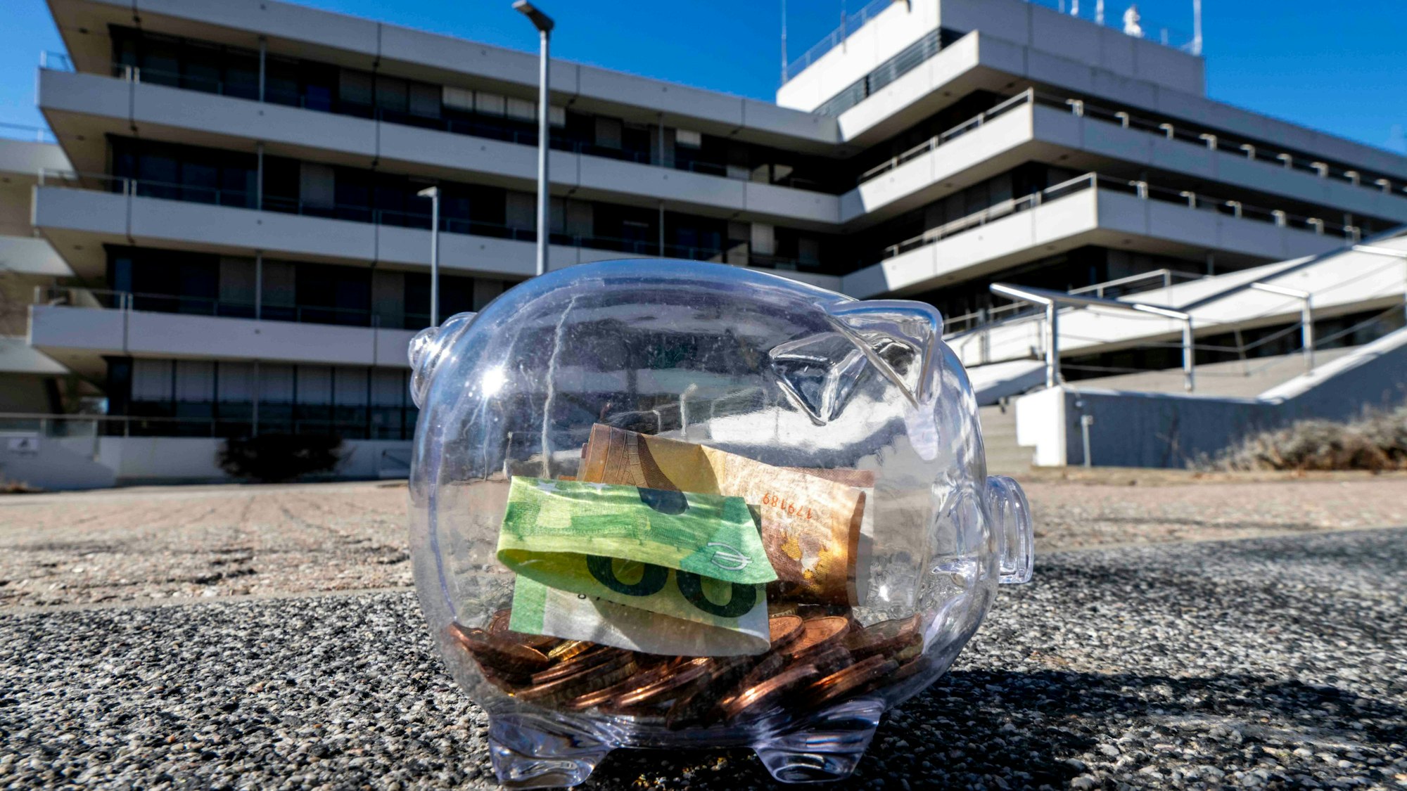 Das Bild zeigt ein Sparschwein auf der Treppe vor dem Kreishaus. Es ist mit Münzen und Scheinen gefüllt.