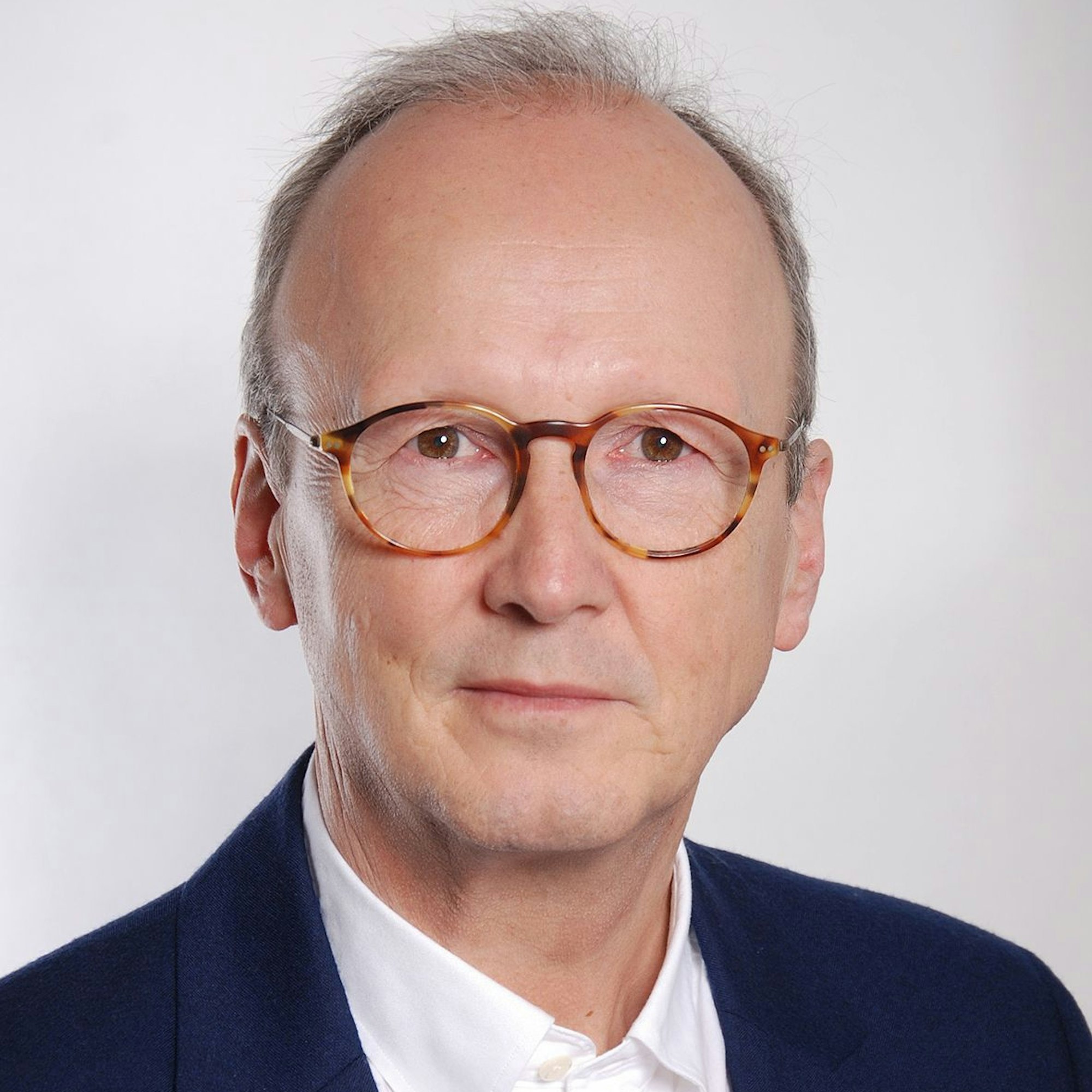 Auf dem Bild ist das Portrait eines Mannes in einem blauen Sakko zu sehen.