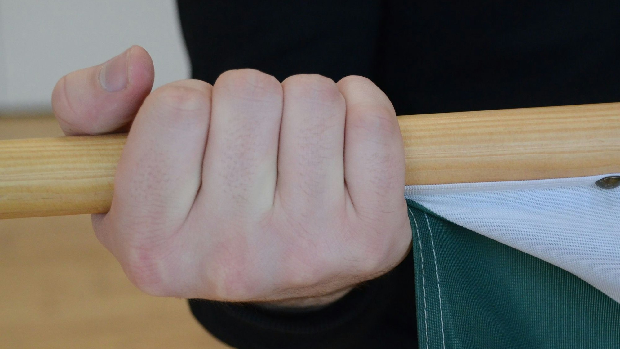 Eine Hand greift einen hölzernen Fahnenstab.