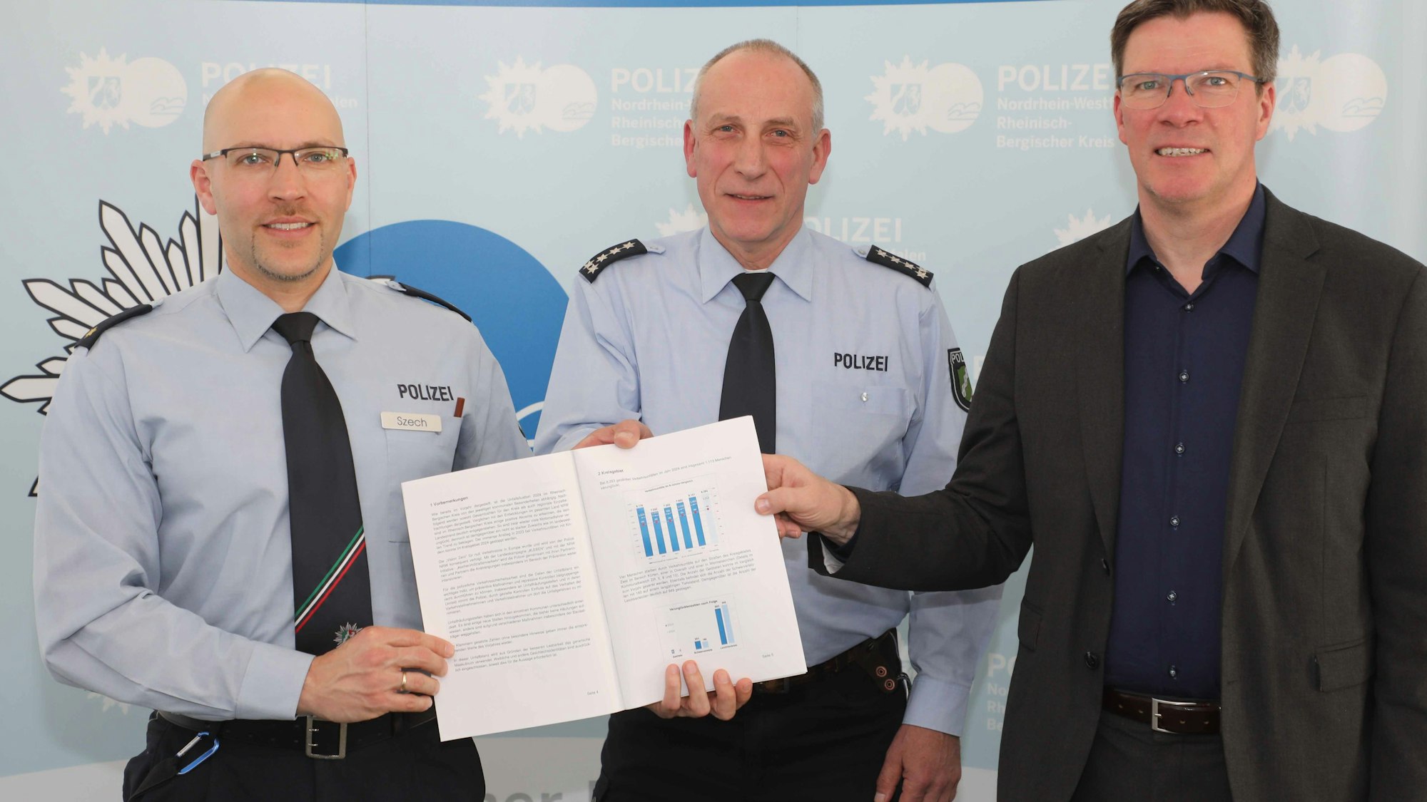 Markus Szech (Leiter Direktion Verkehr), Thomas Schliwitzki (Leiter Verkehrsdienst und Prävention & Opferschutz) und Landrat Stephan Santelmann halten die Verkehrsunfallbilanz für Rhein-Berg 2024.