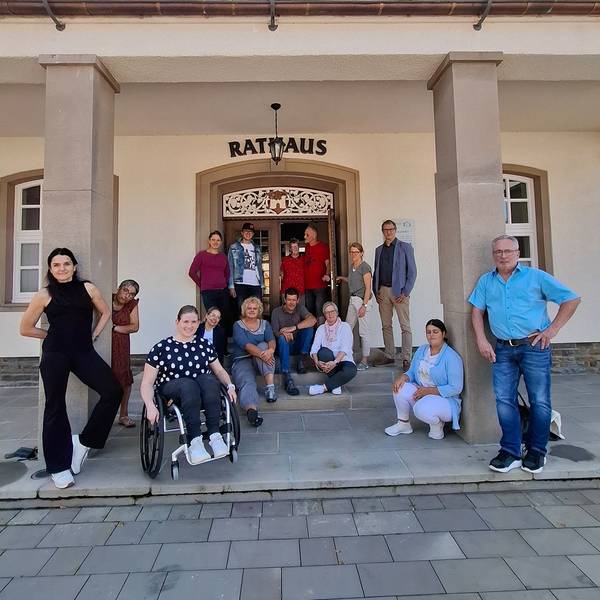 Eine Gruppe von Menschen, darunter eine Frau im Rollstuhl, steht vor dem Rathaus.