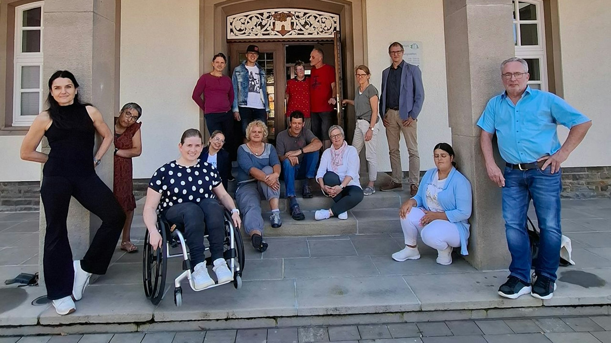 Eine Gruppe von Menschen, darunter eine Frau im Rollstuhl, steht vor dem Rathaus.