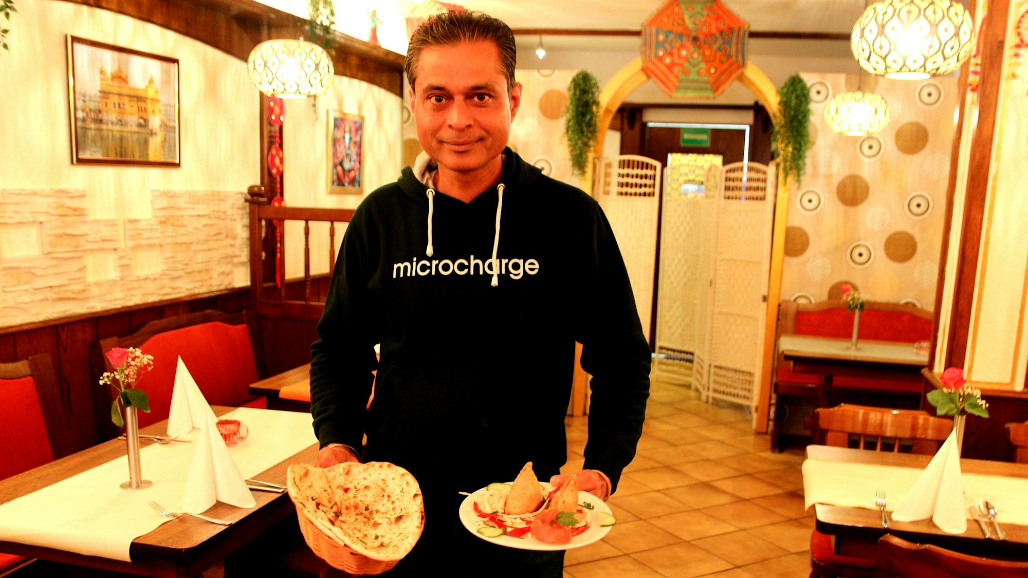 Auf dem Bild ist der Inhaber des neuen Restaurants mit zwei gefüllten Tellern in der Hand zu sehen.