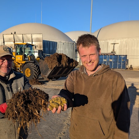 Das Foto zeigt zwei Männer mit vor einem Radlager und den großen Fermentern der Biogasanlage