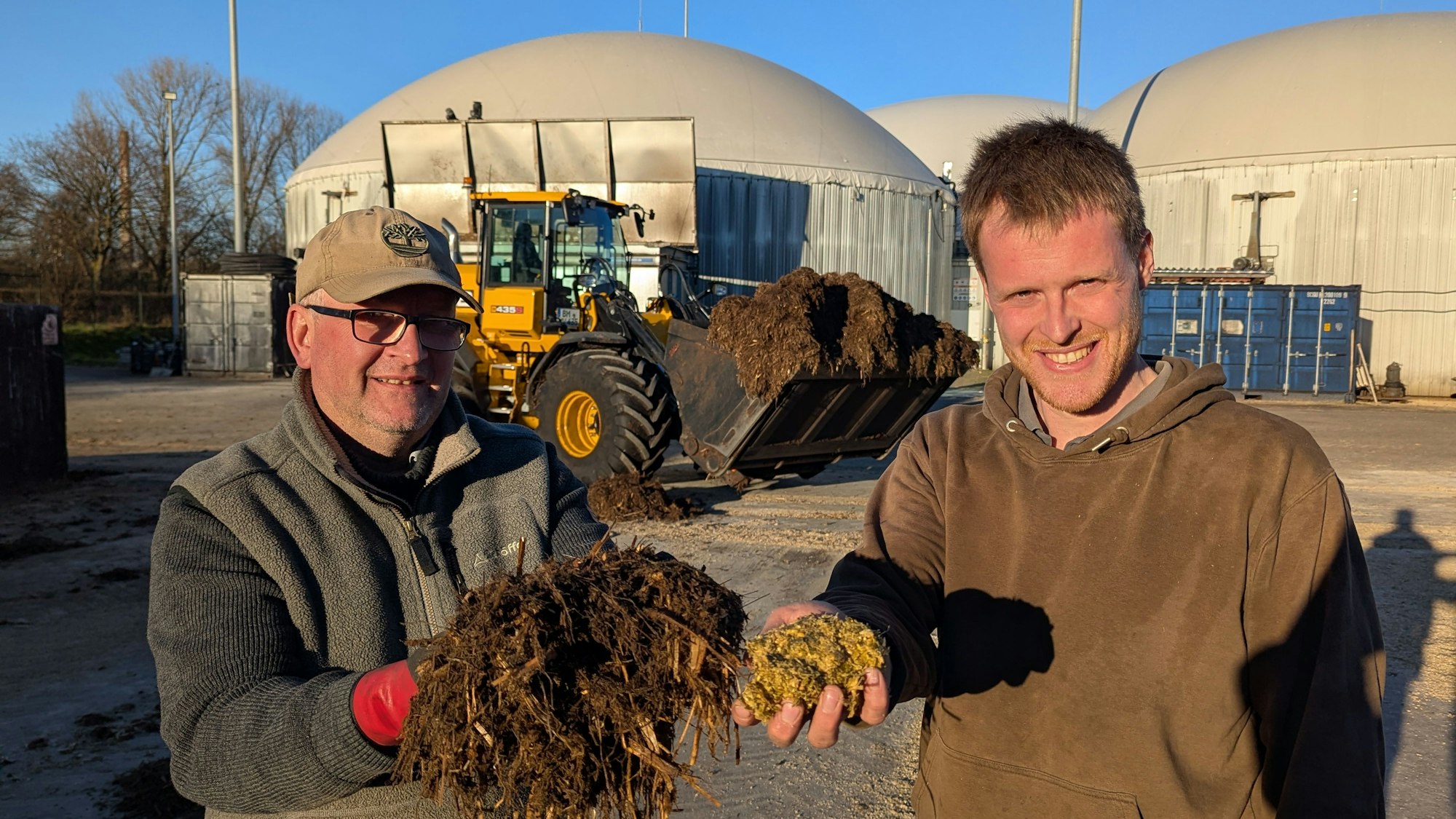Das Foto zeigt zwei Männer mit vor einem Radlager und den großen Fermentern der Biogasanlage