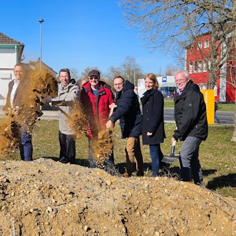 Zu sehen sind mehrere Männer und eine Frau, die mit Spaten an einer Baustelle Erde werfen.